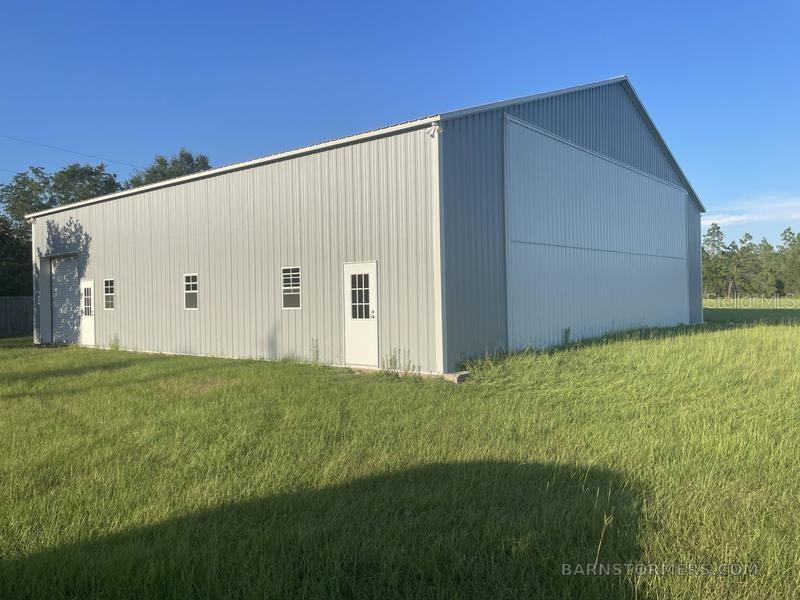 A large, gray metal-sided hangar building stands in a grassy field under a clear sky — 22303 NW LONGLEAF ROAD, FOUNTAIN, FL