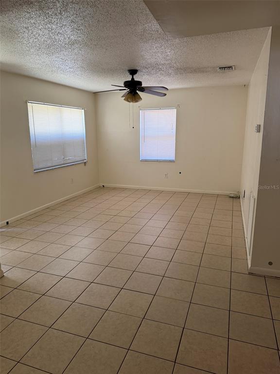 An empty room features beige tile flooring, white walls, two windows, and a ceiling fan — 6458 79TH AVENUE N, PINELLAS PARK, FL
