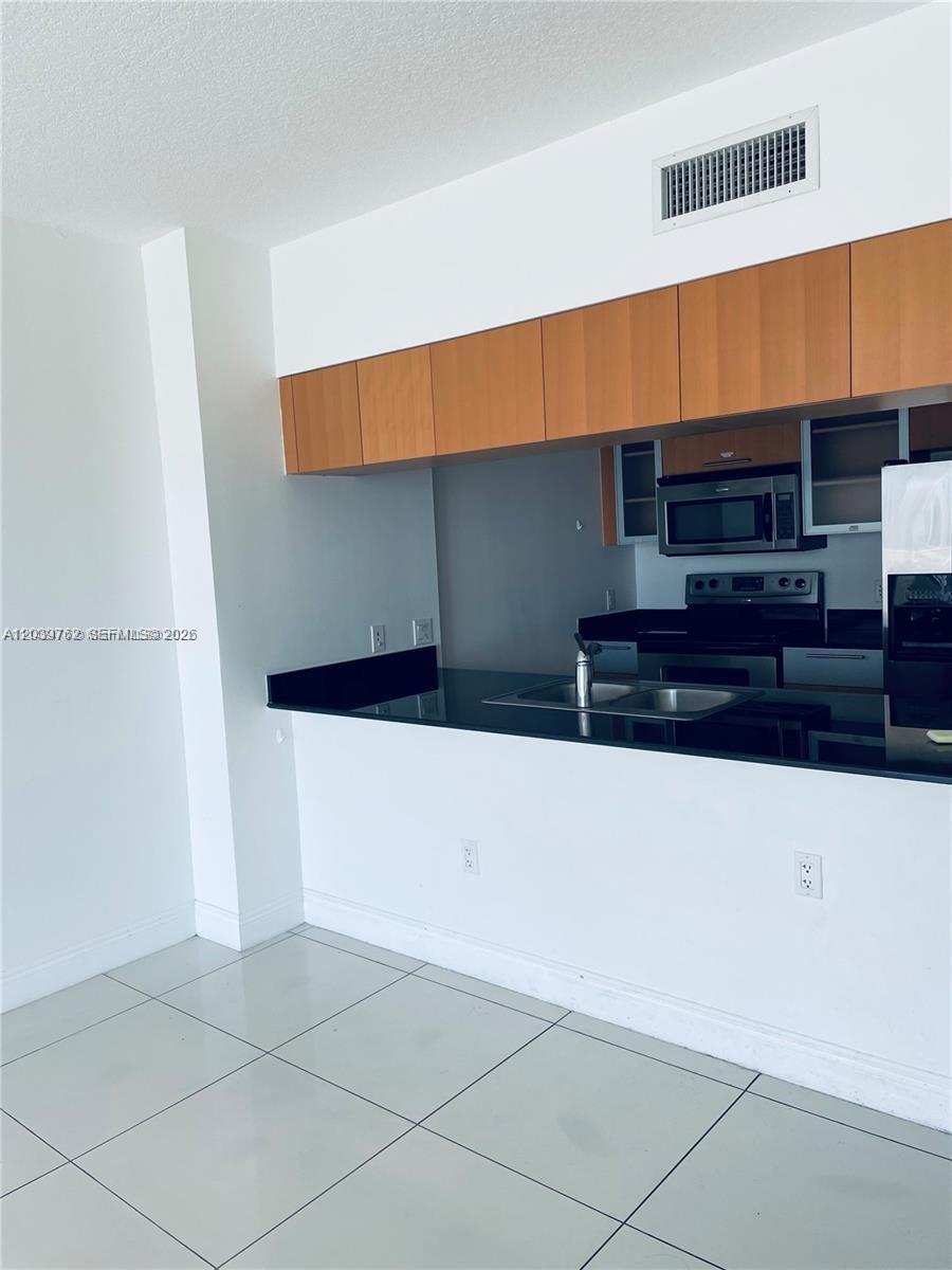 A kitchen features light wood cabinets, black countertops, and white tile flooring — 1750 N Bayshore Dr # 2112, Miami FL 33132, MIAMI, FL