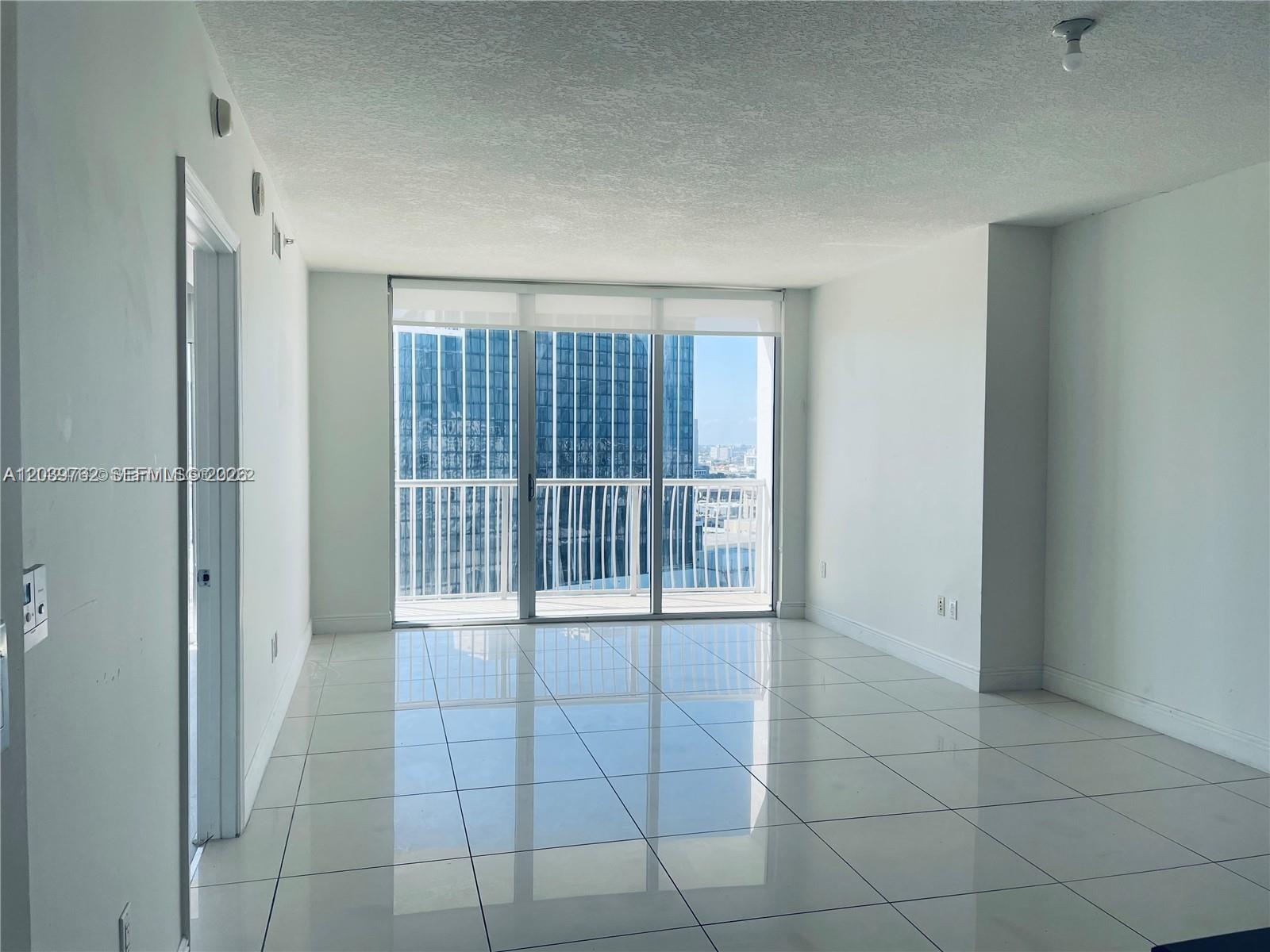An empty room features white tile flooring, white walls, and a sliding glass door to a balcony — 1750 N Bayshore Dr # 2112, Miami FL 33132, MIAMI, FL