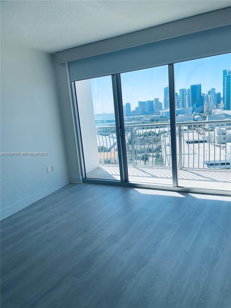 An empty room with light wood-look flooring features a large sliding glass door overlooking a city — 1750 N Bayshore Dr # 2112, Miami FL 33132, MIAMI, FL
