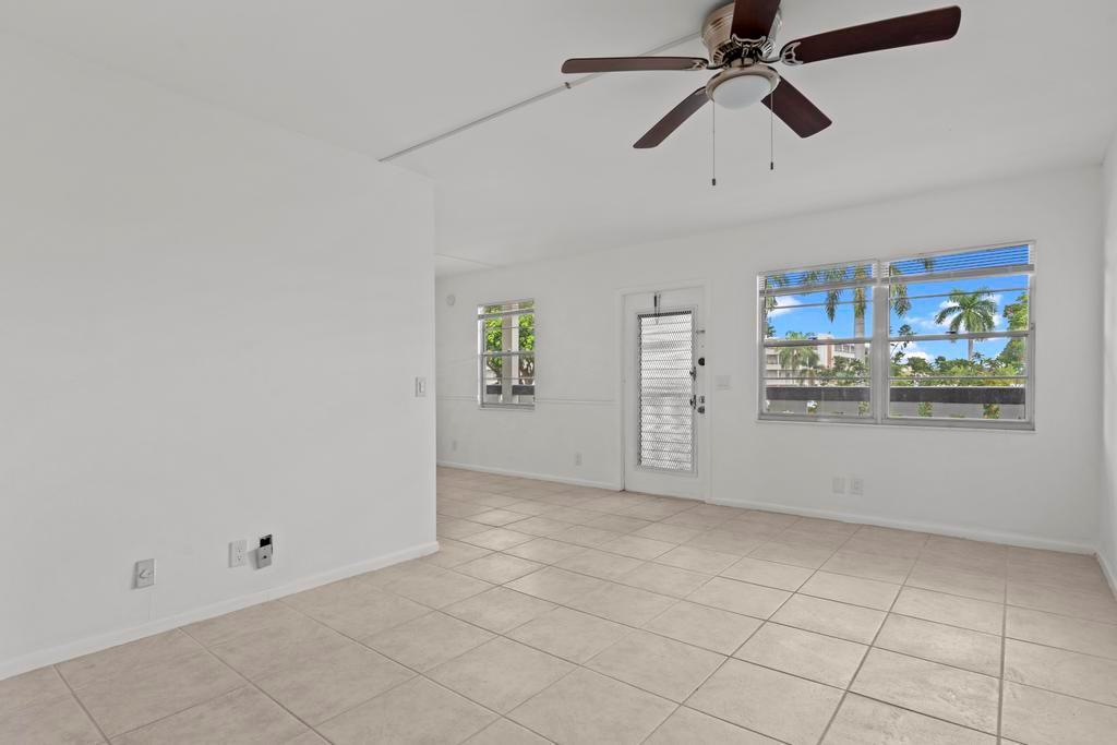 An empty room with white walls, beige tile flooring, a ceiling fan, and large windows — 2044 Hythe C, Boca Raton FL 33434, BOCA RATON, FL