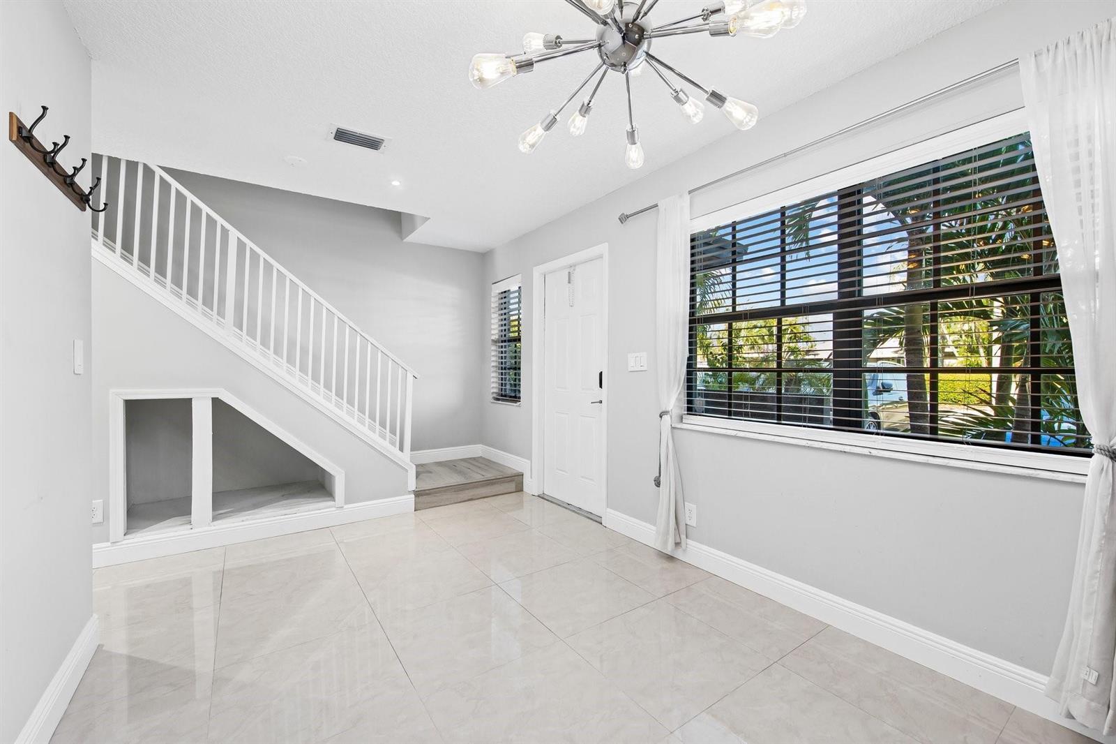 A bright entryway with white walls, tile flooring, a staircase, and a modern chandelier — 2127 NE 11th Avenue, Wilton Manors FL 33305, WILTON MANORS, FL
