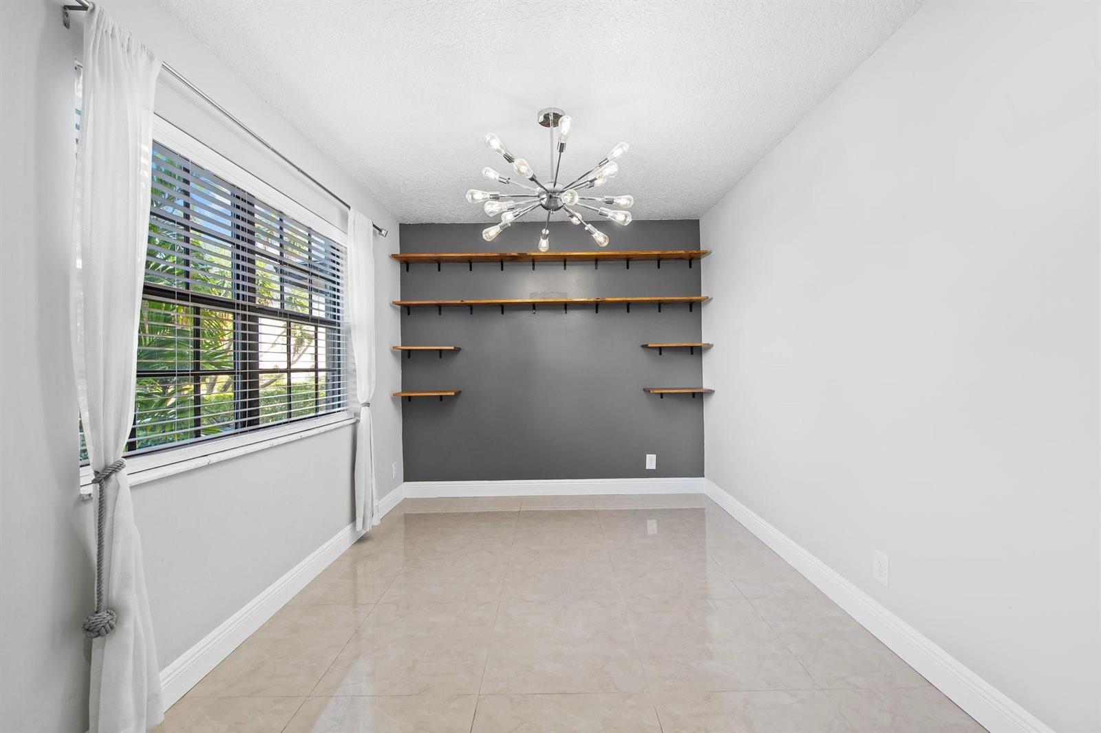 A room with light tile floors, a gray accent wall with shelves, and a chandelier — 2127 NE 11th Avenue, Wilton Manors FL 33305, WILTON MANORS, FL