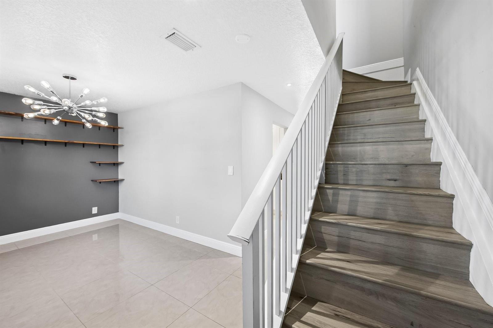 A room with gray tile flooring, a dark accent wall with shelves, and wooden stairs — 2127 NE 11th Avenue, Wilton Manors FL 33305, WILTON MANORS, FL