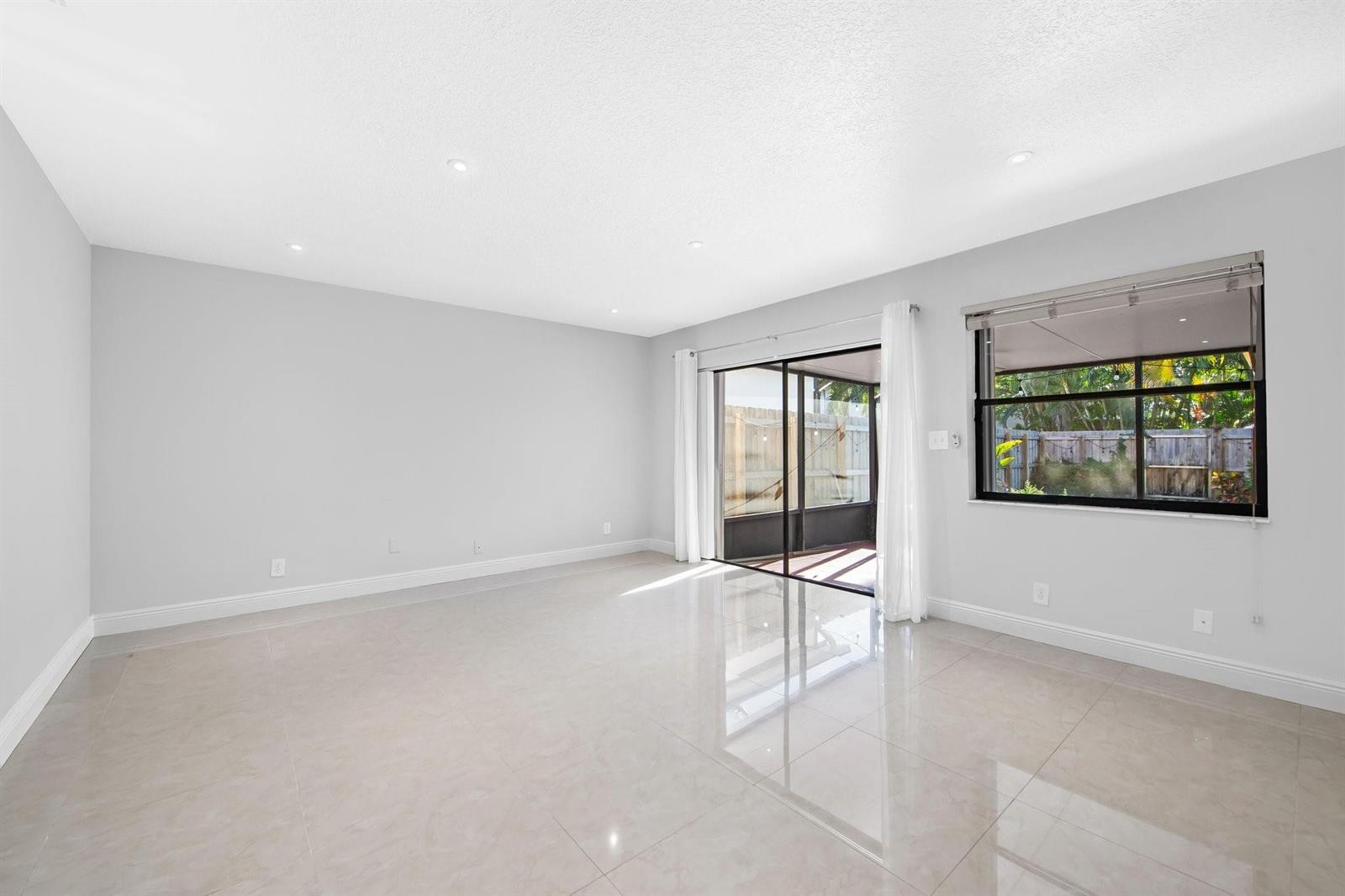 An empty living room with light gray walls, large glossy floor tiles, and sliding glass doors — 2127 NE 11th Avenue, Wilton Manors FL 33305, WILTON MANORS, FL