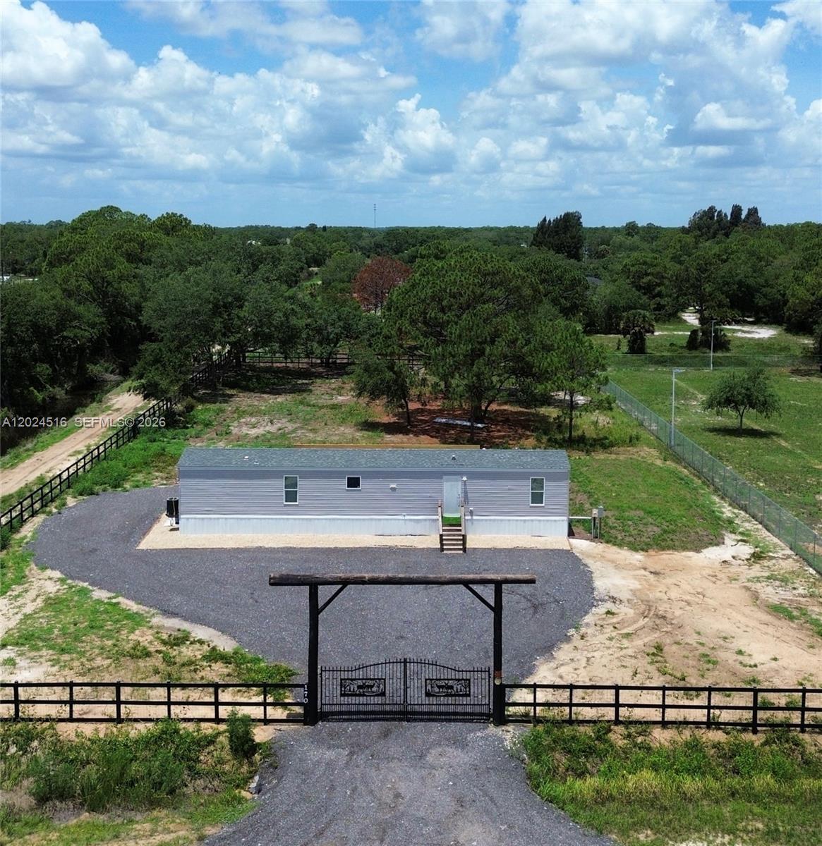 An aerial view shows a single-wide mobile home behind a gated gravel driveway and fence — 170 S Jinete St, Clewiston FL 33440, CLEWISTON, FL