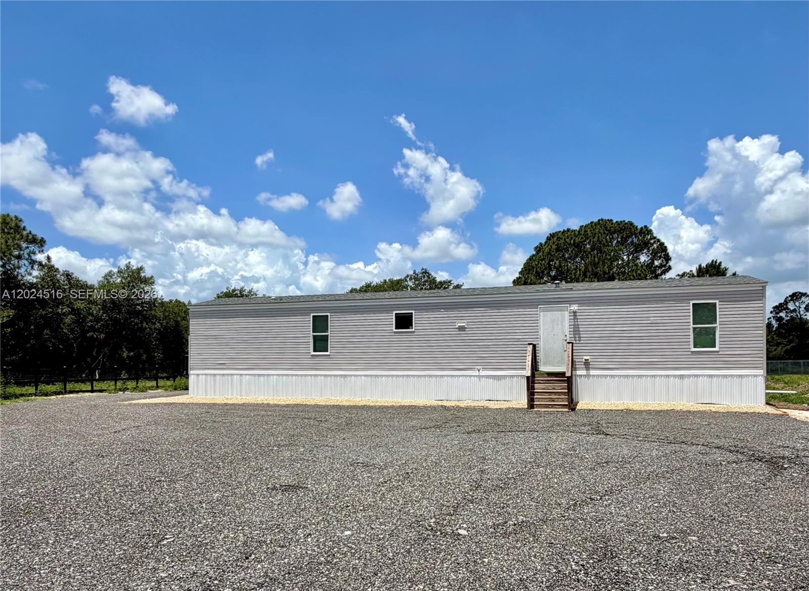 A single-story manufactured home with gray siding sits on a large gravel lot — 170 S Jinete St, Clewiston FL 33440, CLEWISTON, FL