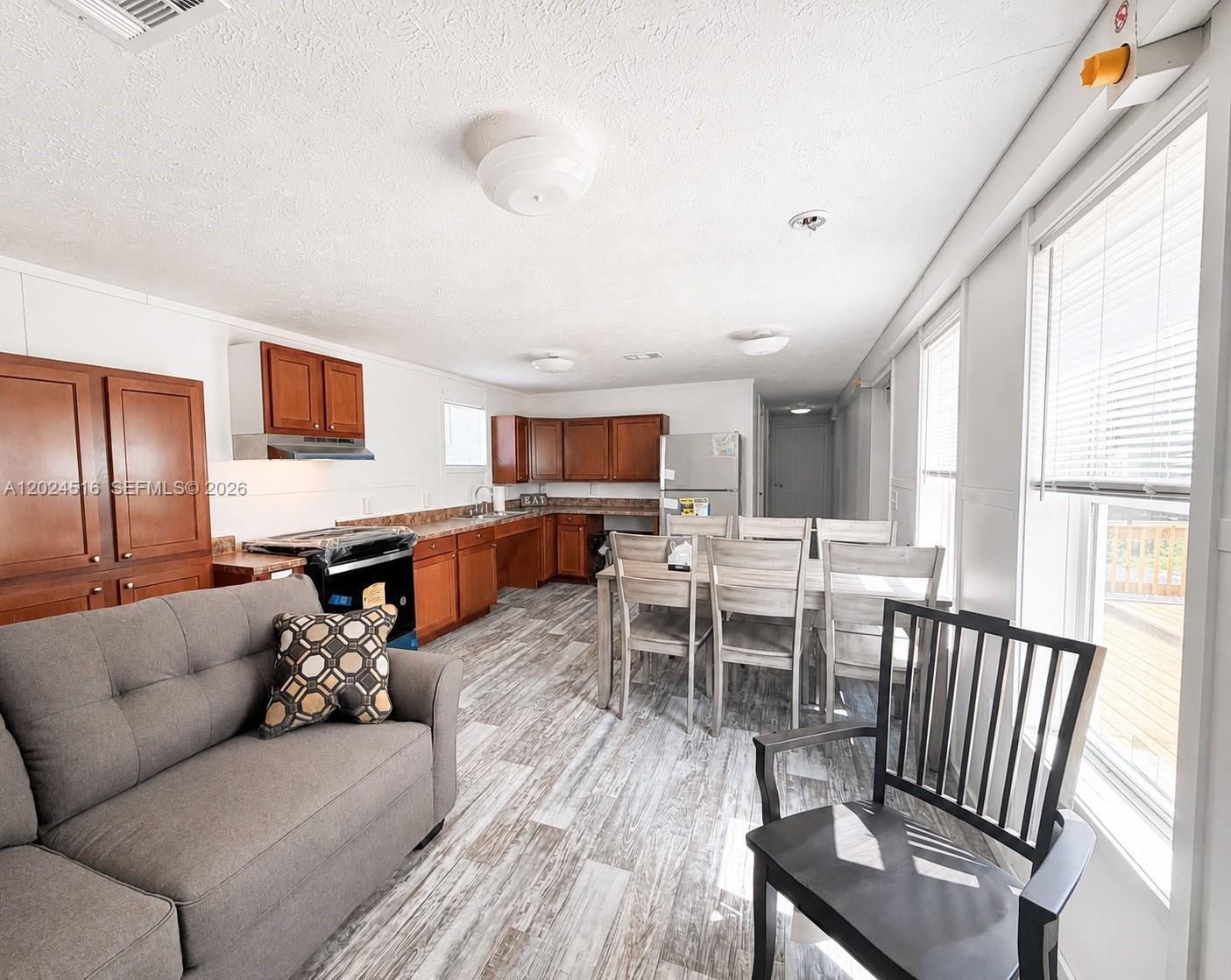 An open-concept kitchen and dining area features wood cabinets, light flooring, and a gray sofa — 170 S Jinete St, Clewiston FL 33440, CLEWISTON, FL