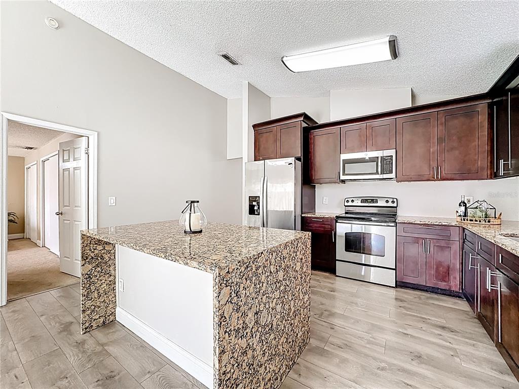 A kitchen features dark wood cabinets, granite countertops, a center island, and stainless steel appliances — 6582 MERITMOOR CIRCLE, ORLANDO, FL