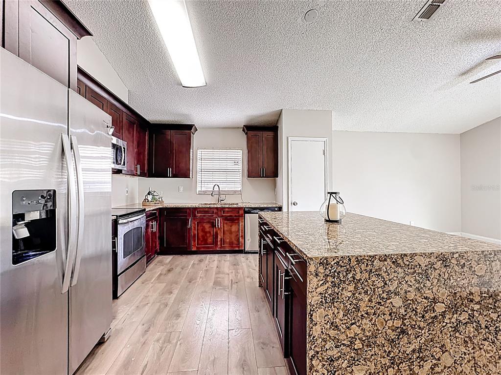 A kitchen features dark wood cabinets, granite countertops, a large island, and stainless steel appliances — 6582 MERITMOOR CIRCLE, ORLANDO, FL