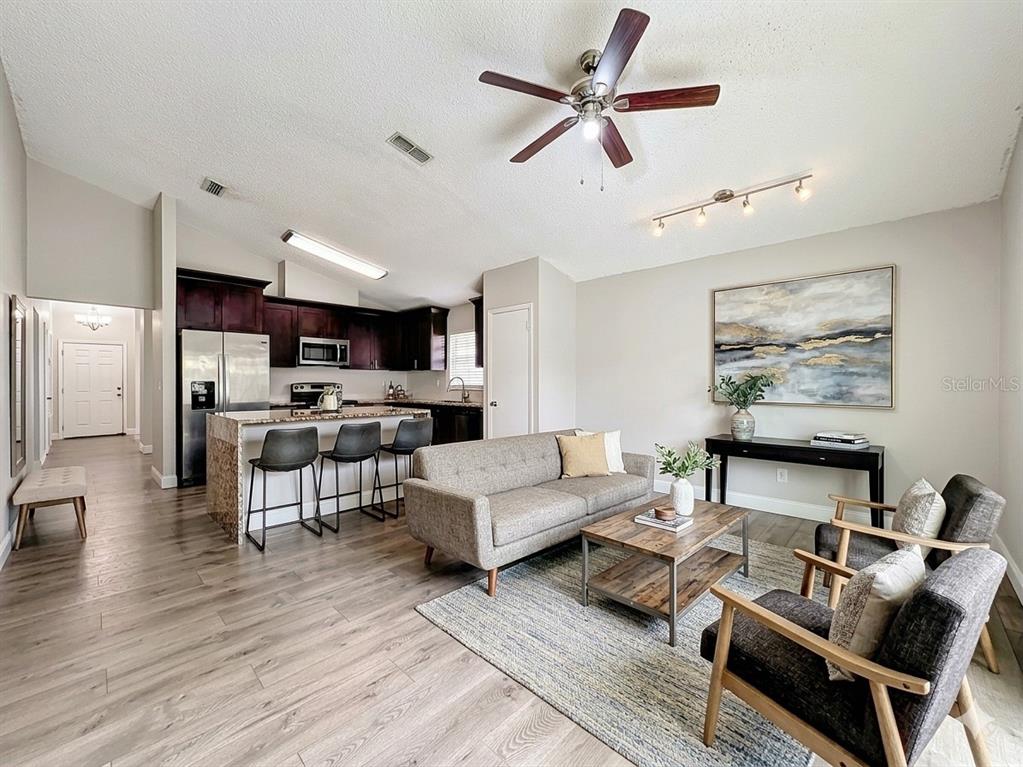 An open-concept living room features a kitchen island, gray sofa, and wood-look flooring — 6582 MERITMOOR CIRCLE, ORLANDO, FL