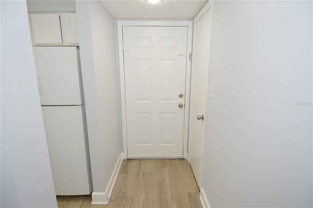 A white refrigerator stands next to a white entry door in a small hallway — 8758 MALLARD RESERVE DRIVE UNIT 101, TAMPA, FL