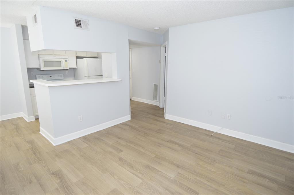 A living room with light-colored walls and wood-look flooring opens to a kitchen area — 8758 MALLARD RESERVE DRIVE UNIT 101, TAMPA, FL