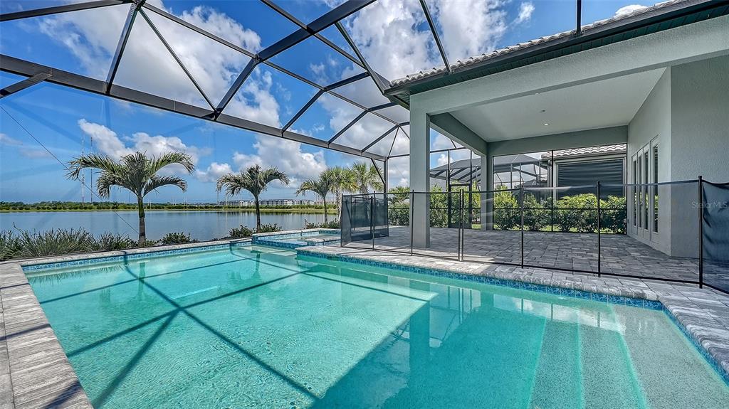 A screened-in swimming pool and patio overlook a lake under a blue sky — 524 BOCELLI DRIVE, NORTH VENICE, FL