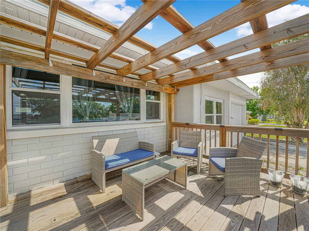A wooden deck features a pergola, wicker patio furniture, and a white brick exterior wall — 231 RIDGE MANOR DRIVE, LAKE WALES, FL