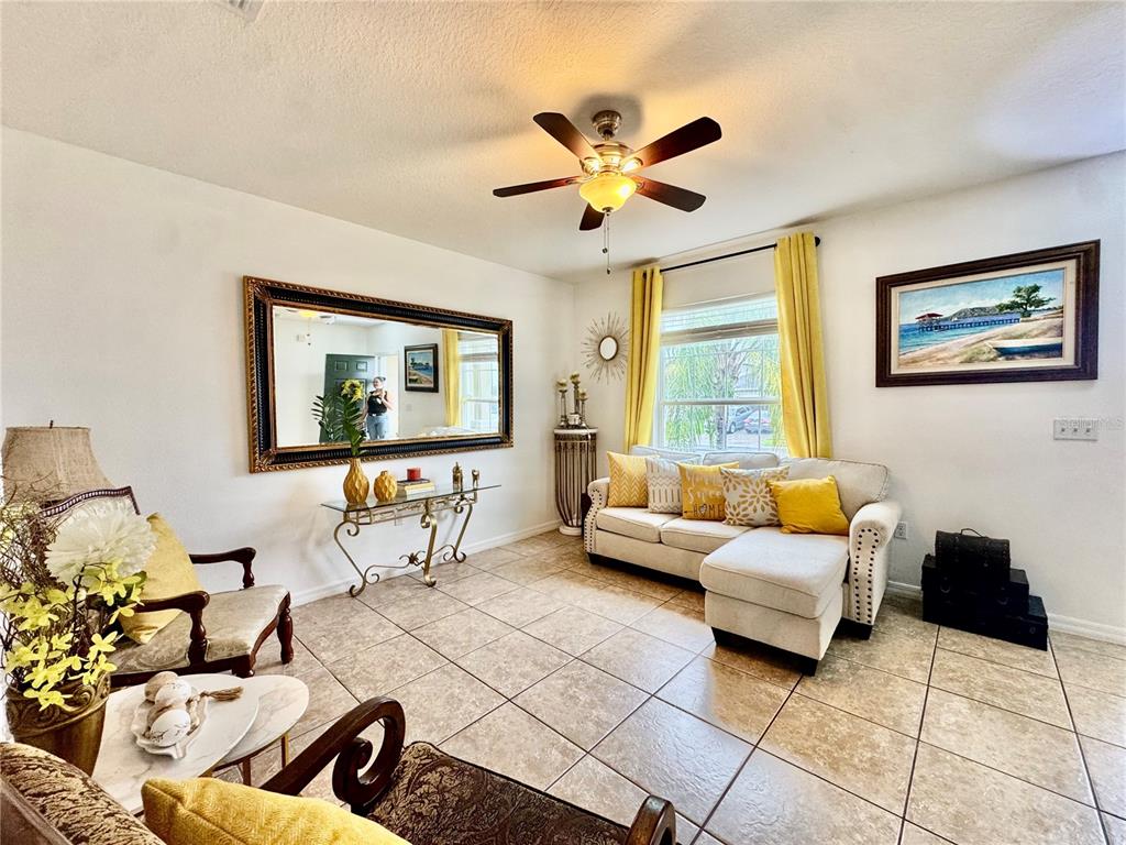 A living room features tile flooring, a beige sectional sofa, a large wall mirror, and yellow accents — 1868 MONTE CRISTO LANE, KISSIMMEE, FL