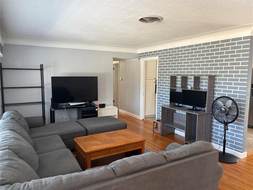 A living room features a gray sectional sofa, a wooden coffee table, and a brick-patterned wall — 6221 13TH AVENUE N, ST PETERSBURG, FL