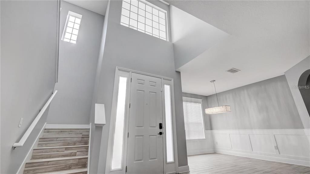 An entryway features a high ceiling, a staircase with wood-look steps, and a white door — 3833 SISKIN DRIVE, KISSIMMEE, FL
