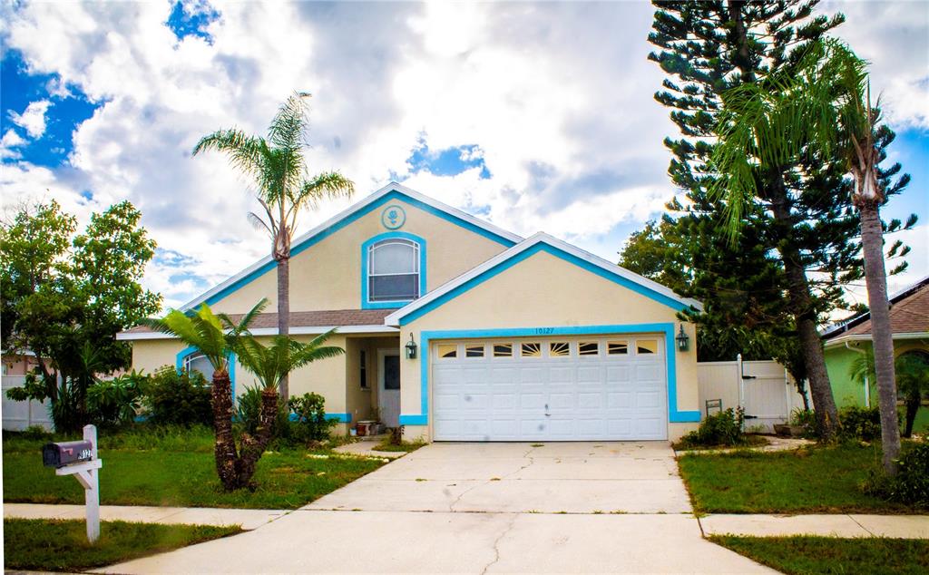 A single-story house with a beige stucco exterior, blue trim, and a two-car garage — 10127 BARNETT LOOP, PORT RICHEY, FL