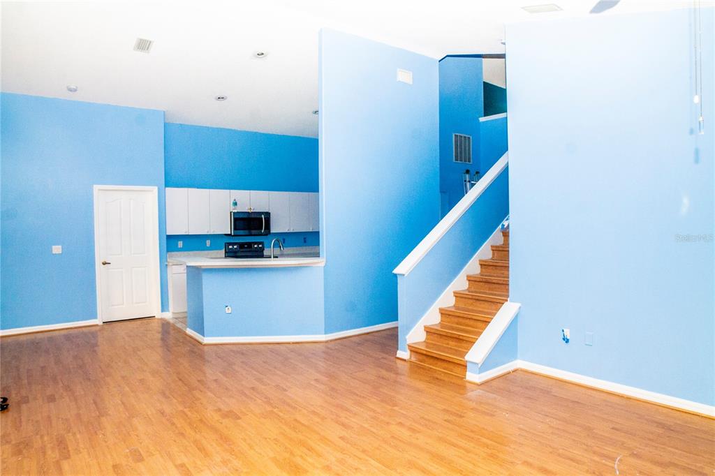 A bright blue room features wood flooring, a kitchen area, and a wooden staircase — 10127 BARNETT LOOP, PORT RICHEY, FL