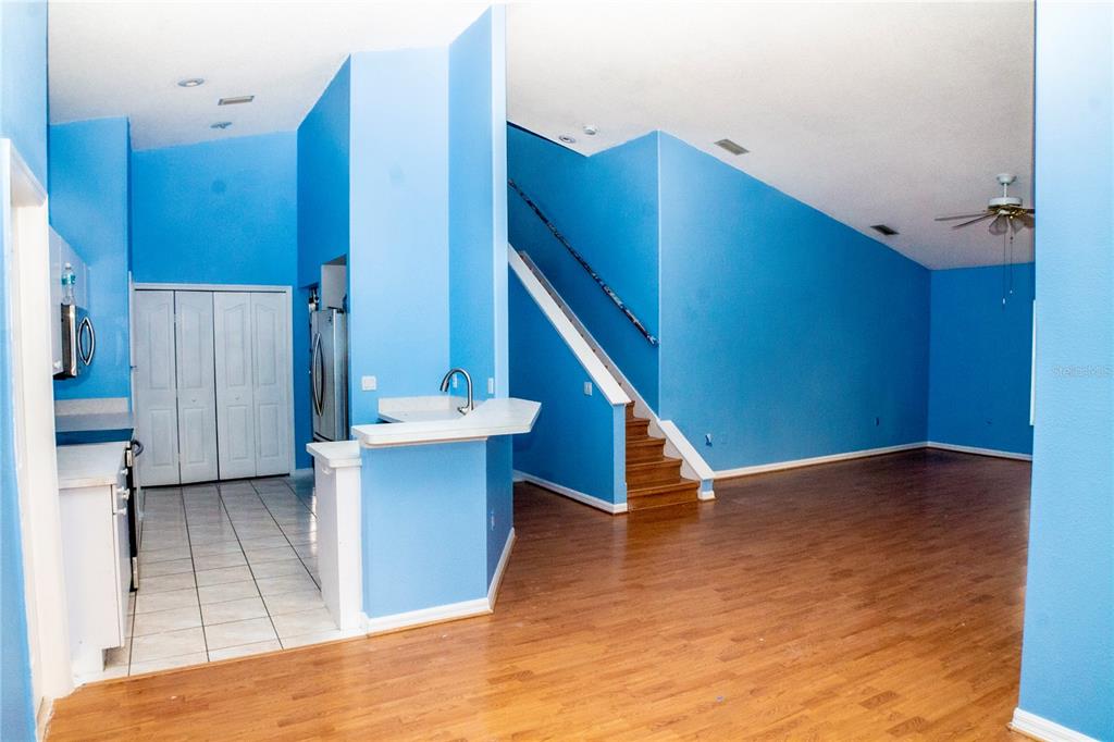 An open-concept living area with blue walls, wood flooring, a kitchen, and a staircase — 10127 BARNETT LOOP, PORT RICHEY, FL