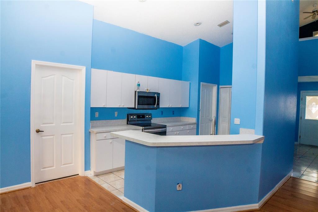A kitchen features blue walls, white cabinets, a breakfast bar, and light-colored countertops — 10127 BARNETT LOOP, PORT RICHEY, FL