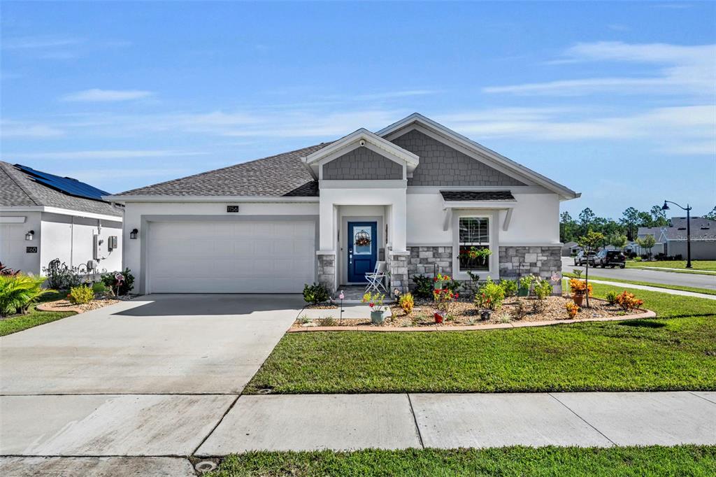 A single-story suburban house with a two-car garage, stone accents, and a blue front door — 1156 SAND TRAP COURT, DAYTONA BEACH, FL