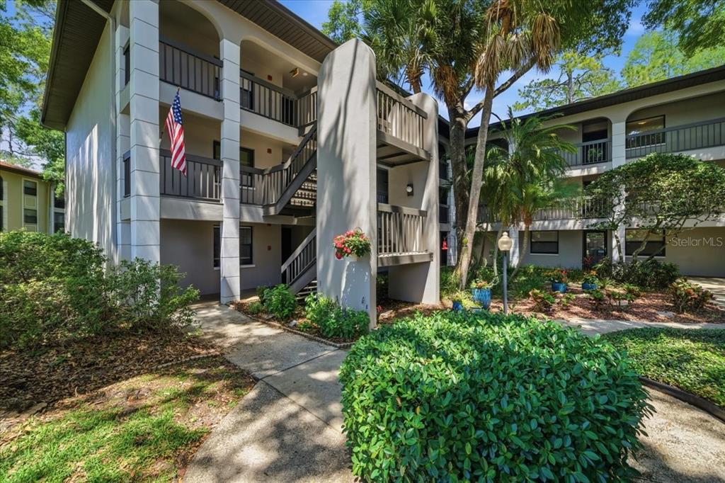 A three-story apartment building exterior with a central staircase and a landscaped courtyard — 3399 MERMOOR DRIVE UNIT 101, PALM HARBOR, FL
