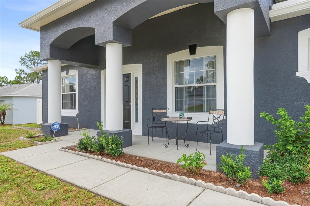 A dark gray house exterior features a covered front porch with white columns and furniture — 11436 LAGORCE AVENUE, SPRING HILL, FL