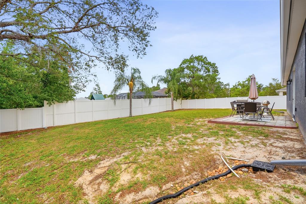 A fenced backyard features a small paved patio with outdoor furniture and sparse grass — 11436 LAGORCE AVENUE, SPRING HILL, FL