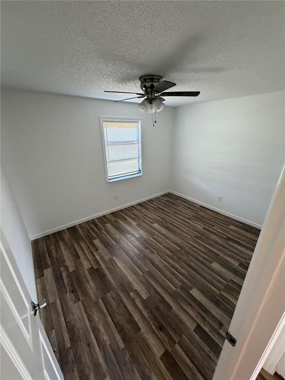 An empty bedroom with white walls, a ceiling fan, and dark wood-look laminate flooring — 11748 OCEANSPRAY BOULEVARD, ENGLEWOOD, FL
