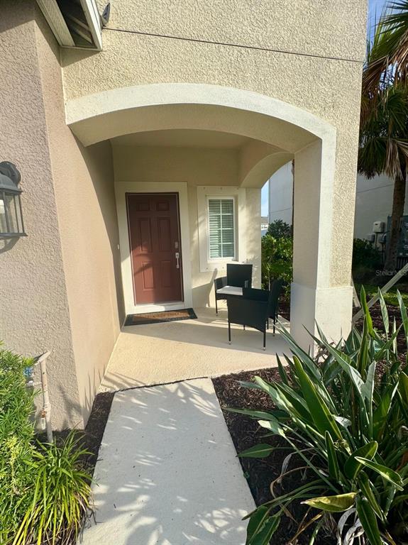A covered entryway features a brown front door, two black chairs, and a concrete walkway — 5715 ARCHIPELAGO STREET, NOKOMIS, FL