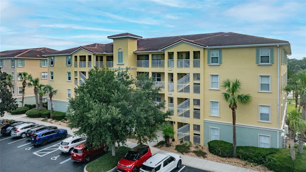 An exterior view of a multi-story yellow apartment building with a parking lot in front — 700 CANOPY WALK LANE UNIT 723, PALM COAST, FL