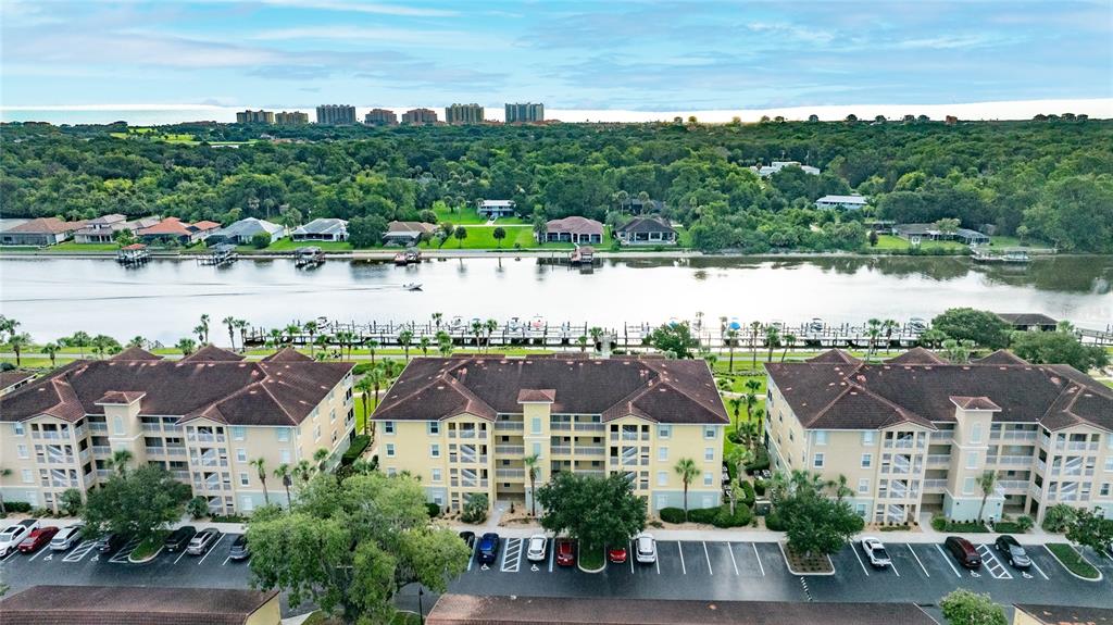 An aerial view shows three multi-story apartment buildings with parking lots beside a river — 700 CANOPY WALK LANE UNIT 723, PALM COAST, FL