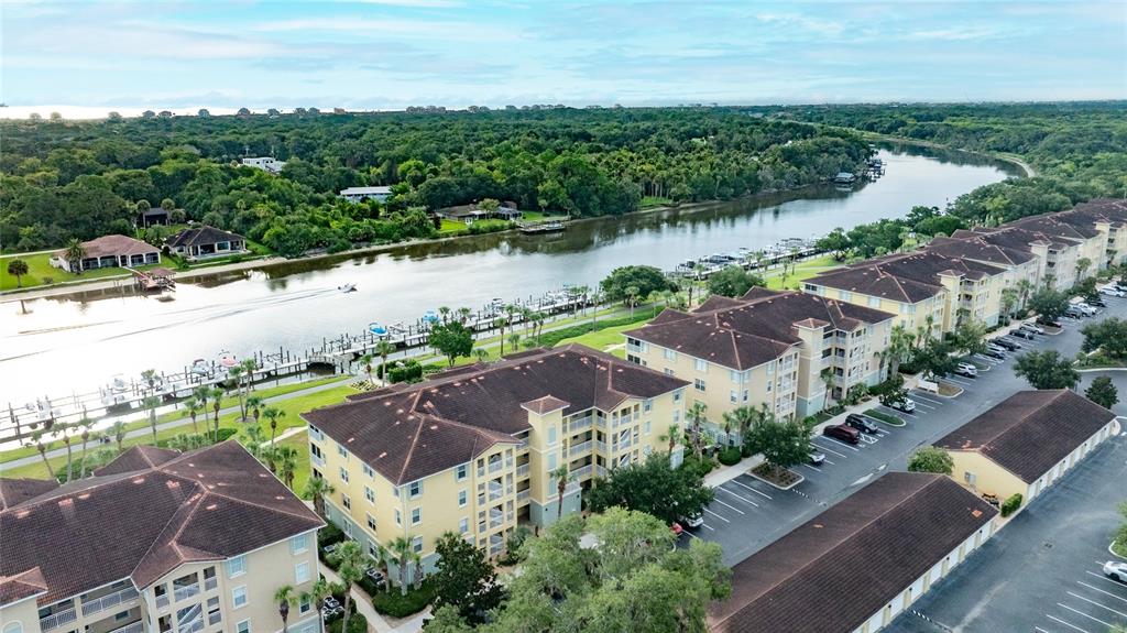 An aerial view shows multi-story apartment buildings with brown roofs situated along a river — 700 CANOPY WALK LANE UNIT 723, PALM COAST, FL