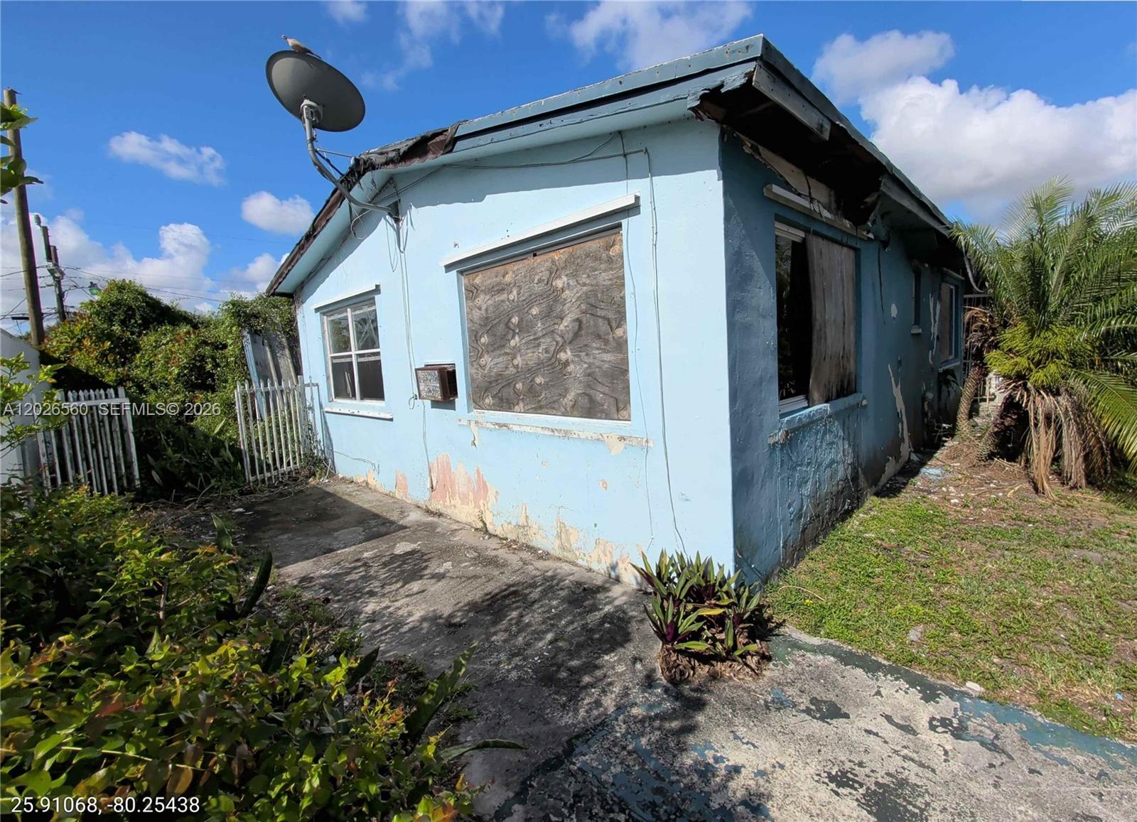 A weathered, light blue house features boarded-up windows and a satellite dish on the roof — 820 Curtiss Dr, Opa-Locka FL 33054, OPA-LOCKA, FL