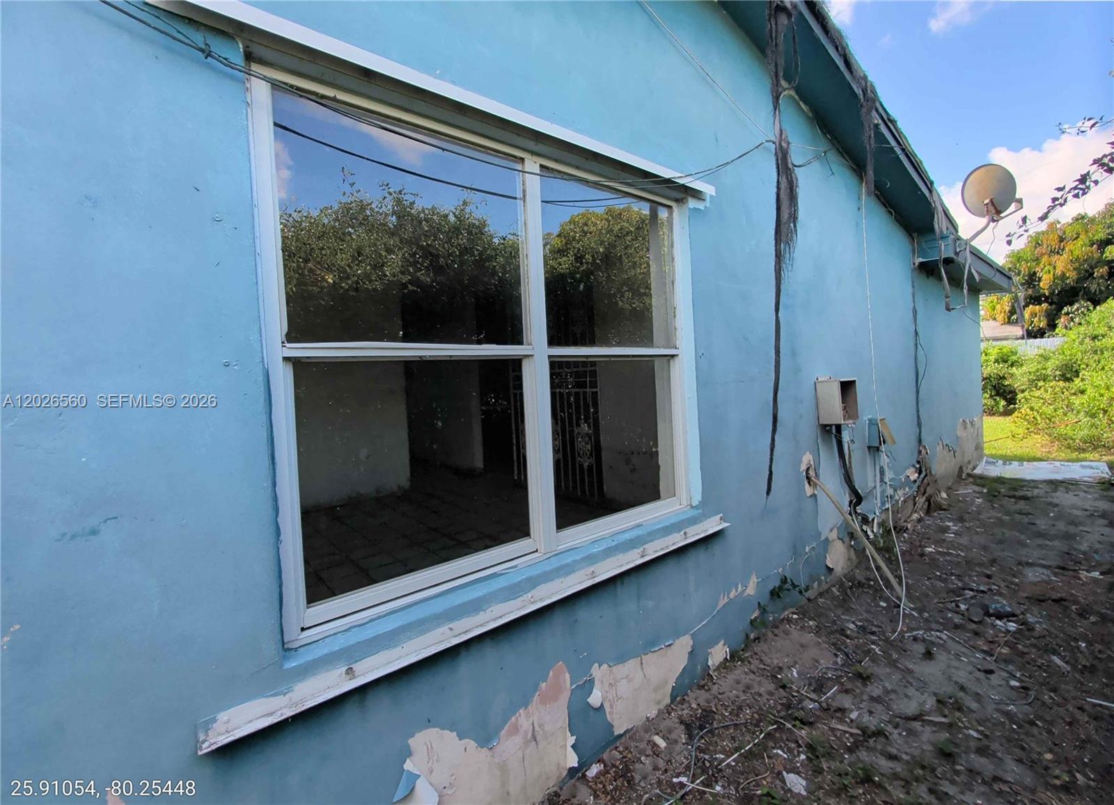 The exterior of a blue house shows a window, peeling paint, and exposed wiring — 820 Curtiss Dr, Opa-Locka FL 33054, OPA-LOCKA, FL
