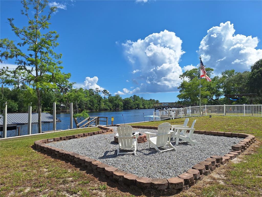A gravel fire pit area with white chairs overlooks a river and a boat dock — 8213 RIVERVIEW ROAD, FANNING SPRINGS, FL