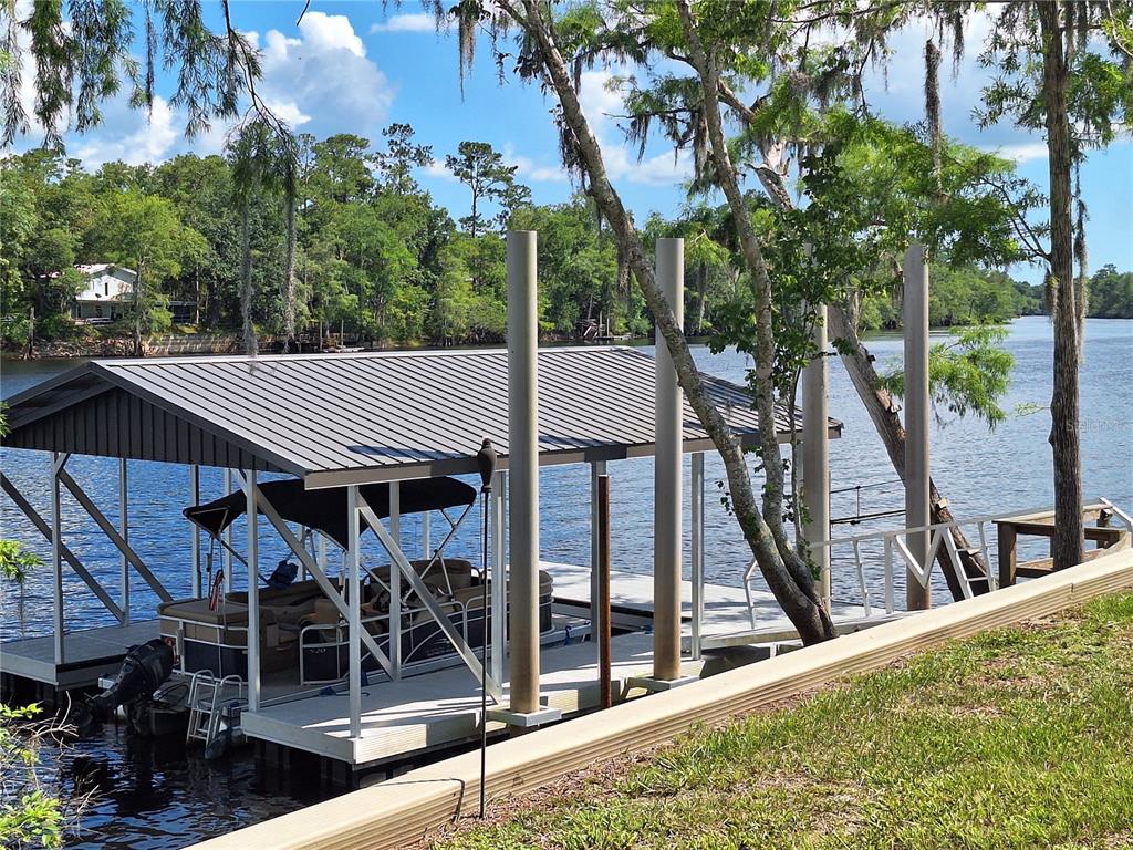 A boat dock with a metal roof sits on a river next to a grassy bank — 8213 RIVERVIEW ROAD, FANNING SPRINGS, FL