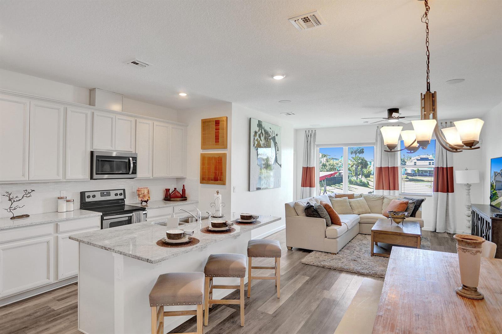 An open-concept kitchen and living area features white cabinetry, granite countertops, and wood-look flooring — 1905 Vernon Street, FL 33460, FL