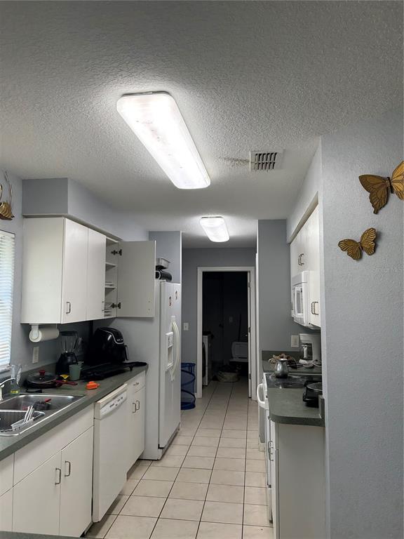 A galley-style kitchen features white cabinets, light countertops, tile flooring, and two ceiling lights — 10013 OSLIN STREET, TAMPA, FL