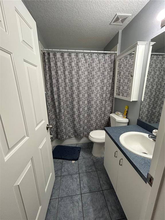 A small bathroom features a white vanity, a toilet, and a shower with a patterned curtain — 10013 OSLIN STREET, TAMPA, FL