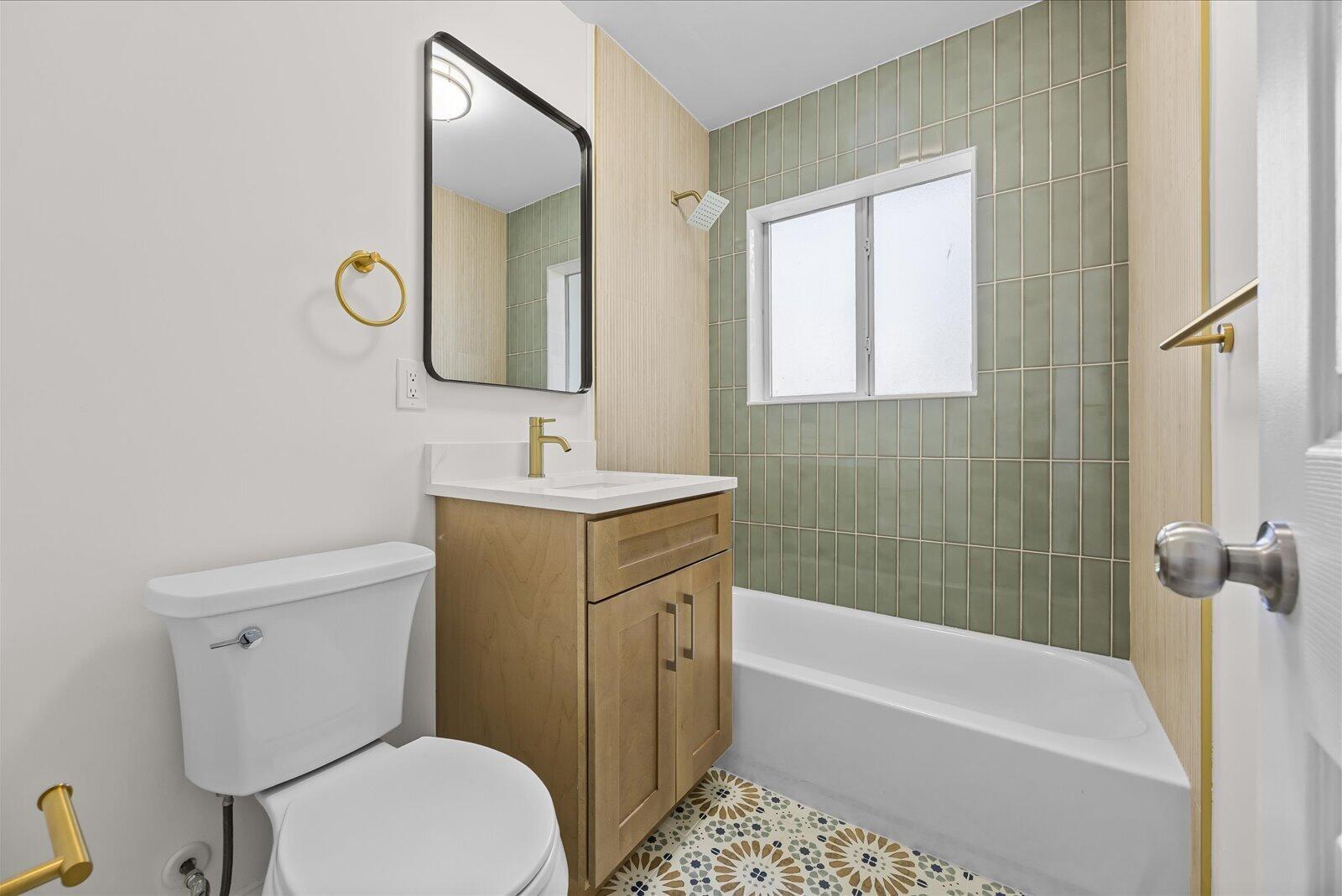 A bathroom features a wood vanity, a green tiled shower wall, and patterned floor tiles — 800 SE 13th Court, Deerfield Beach FL 33441, DEERFIELD BEACH, FL