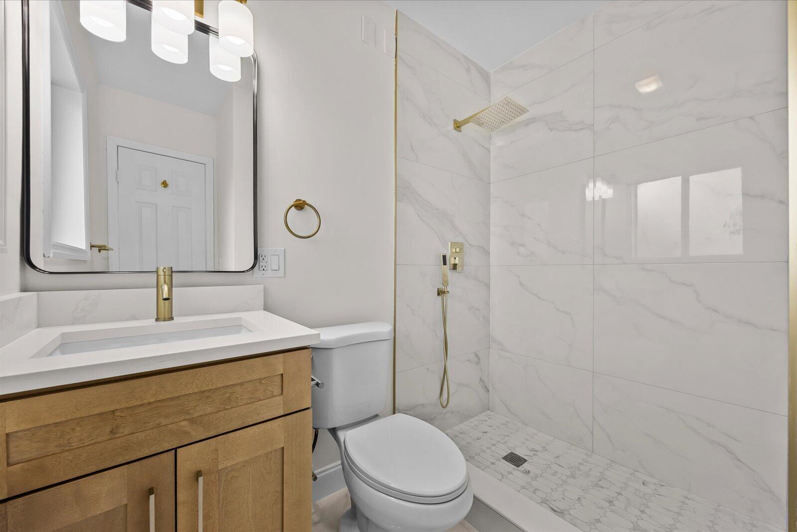 A bathroom features a wood vanity, white toilet, and a walk-in shower with marble-look tiles — 800 SE 13th Court, Deerfield Beach FL 33441, DEERFIELD BEACH, FL