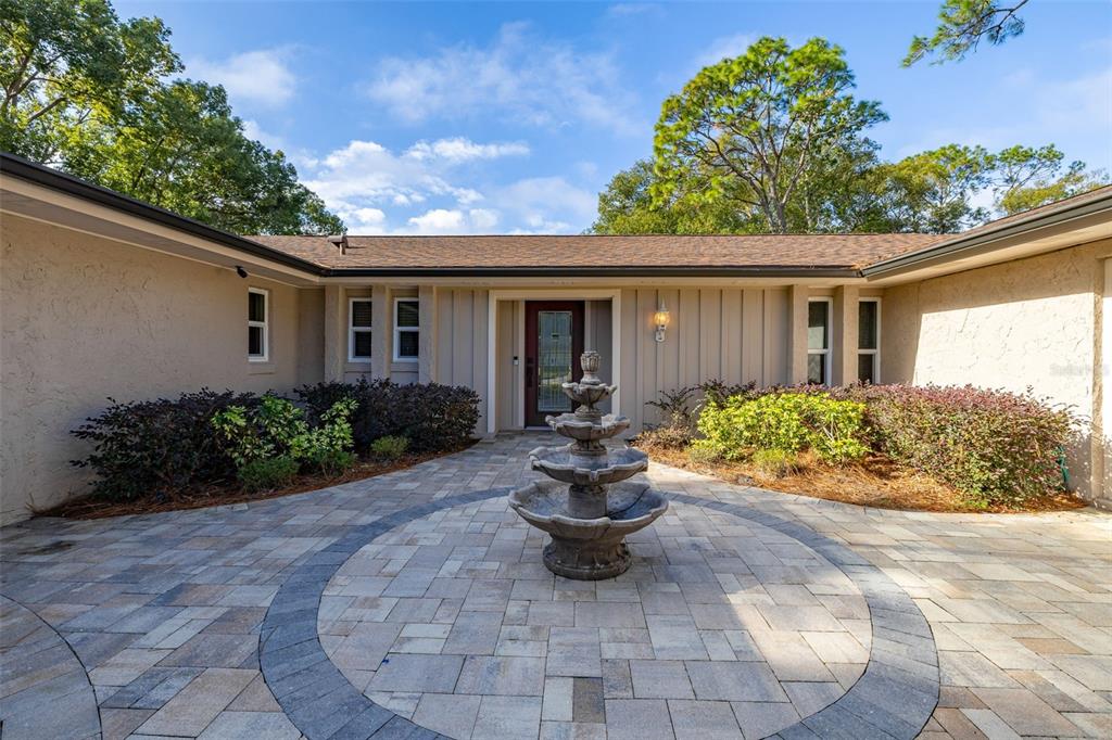 A stone fountain sits in the center of a paved courtyard leading to a house entrance — 204 BLUE LAKE DRIVE, LONGWOOD, FL