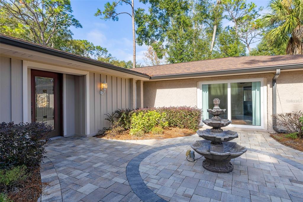 A stone-paved courtyard features a tiered fountain in front of a house with siding — 204 BLUE LAKE DRIVE, LONGWOOD, FL