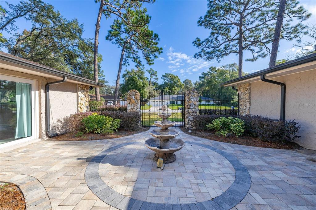 A stone-paved courtyard features a tiered fountain between two building wings and a gated entrance — 204 BLUE LAKE DRIVE, LONGWOOD, FL