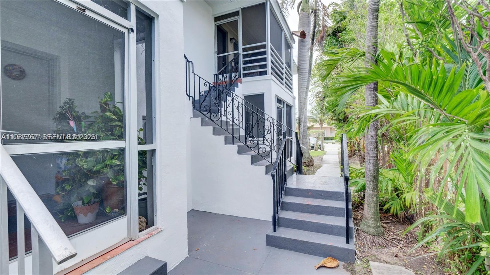 An exterior view shows a white building with a screened balcony and metal stairs — 1791 Marseille Dr, Miami Beach FL 33141, MIAMI BEACH, FL