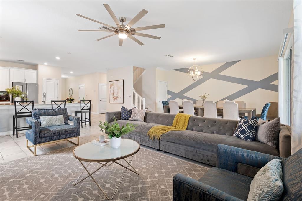 An open-concept living and dining area features a large gray sectional, patterned rug, and accent wall — 9050 STINGER DRIVE, DAVENPORT, FL